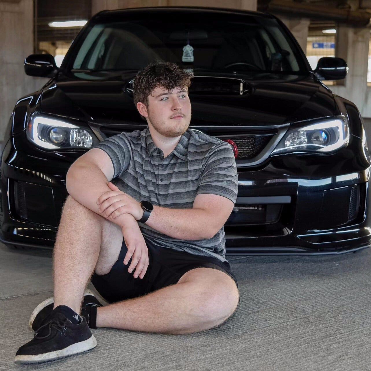 A man is sitting on the ground in front of a black car
