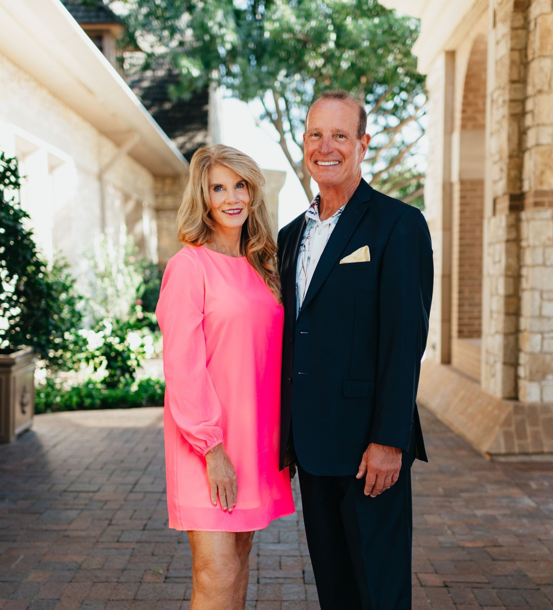 A man in a suit and a woman in a pink dress are posing for a picture.