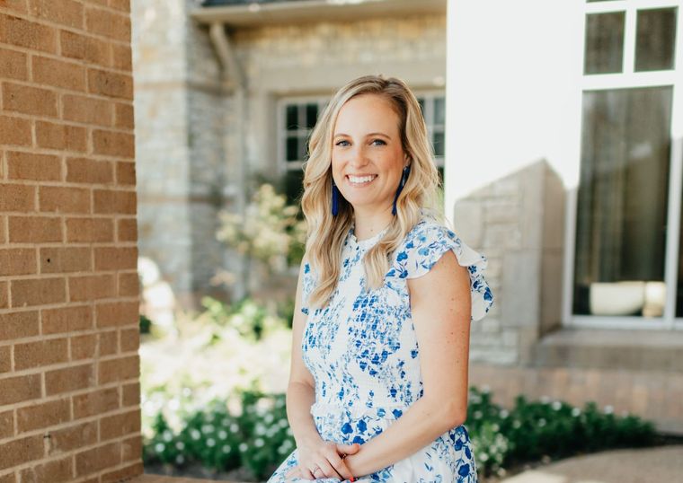 A woman in a blue and white dress is standing in front of a brick building.