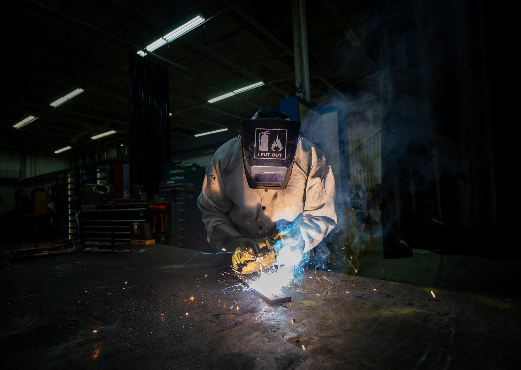 A man is welding a piece of metal in a dark room.