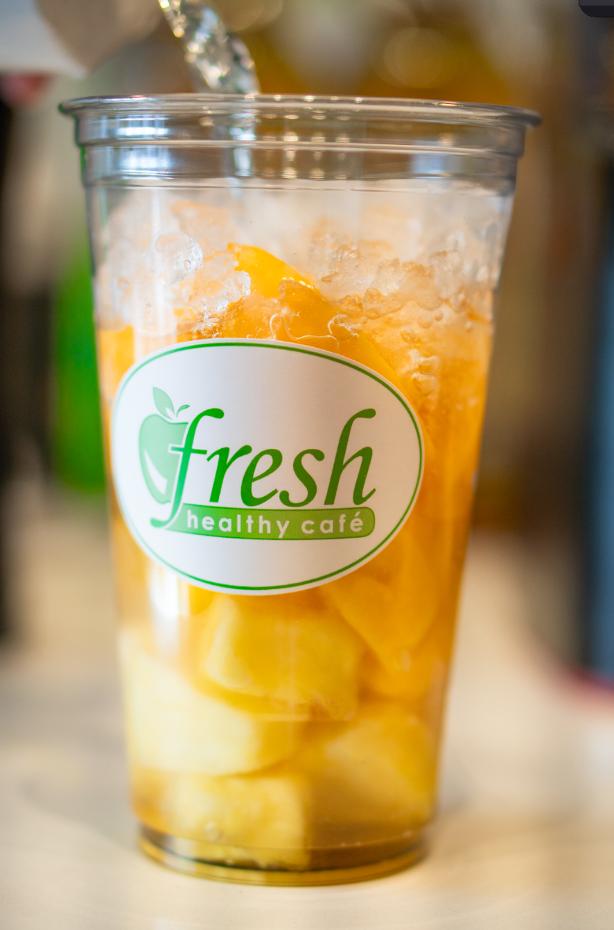 A cup of iced tea with pineapple slices is being poured into it.