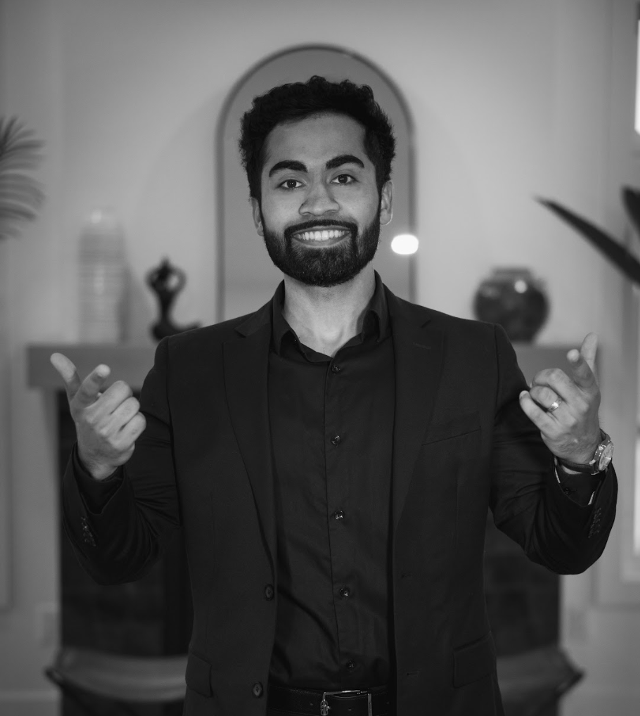 A man in a suit and black shirt is giving a thumbs up in a black and white photo.