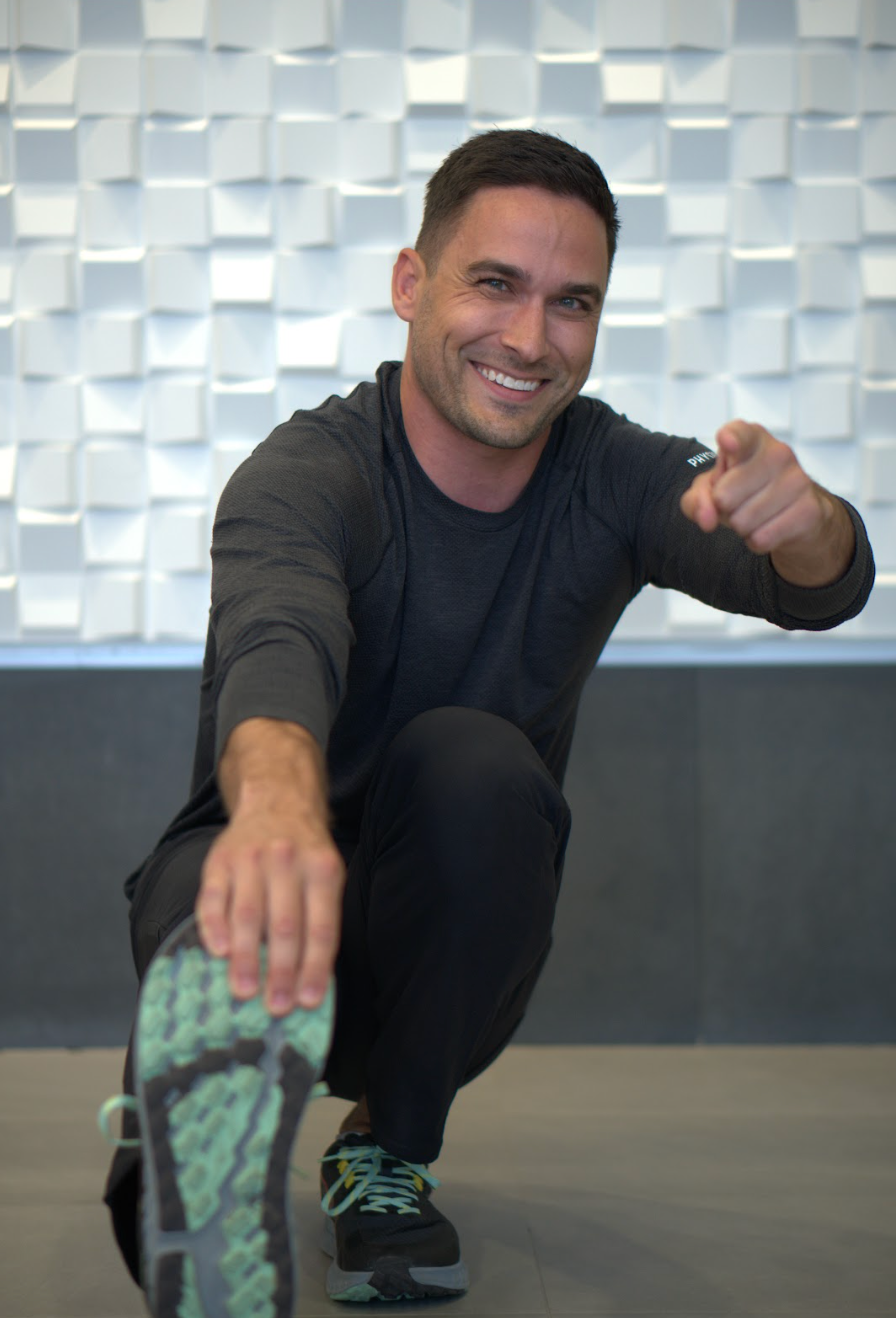 A man is squatting down and pointing at the camera.