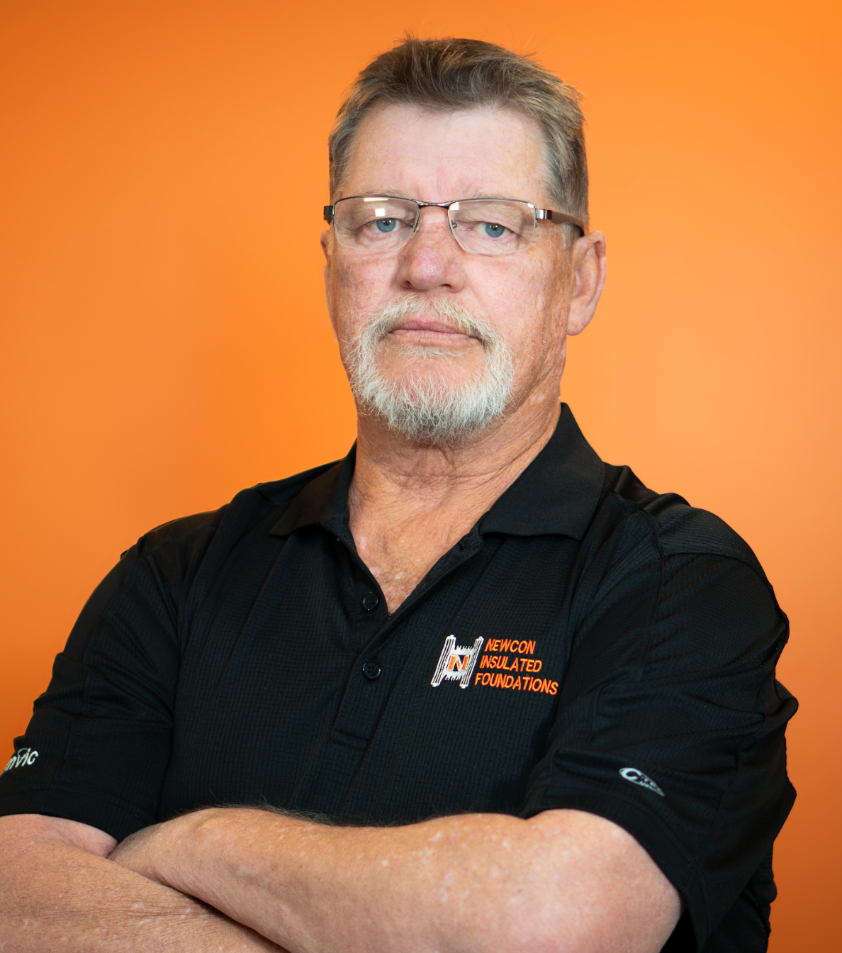 A man with a beard and glasses is wearing a black polo shirt.