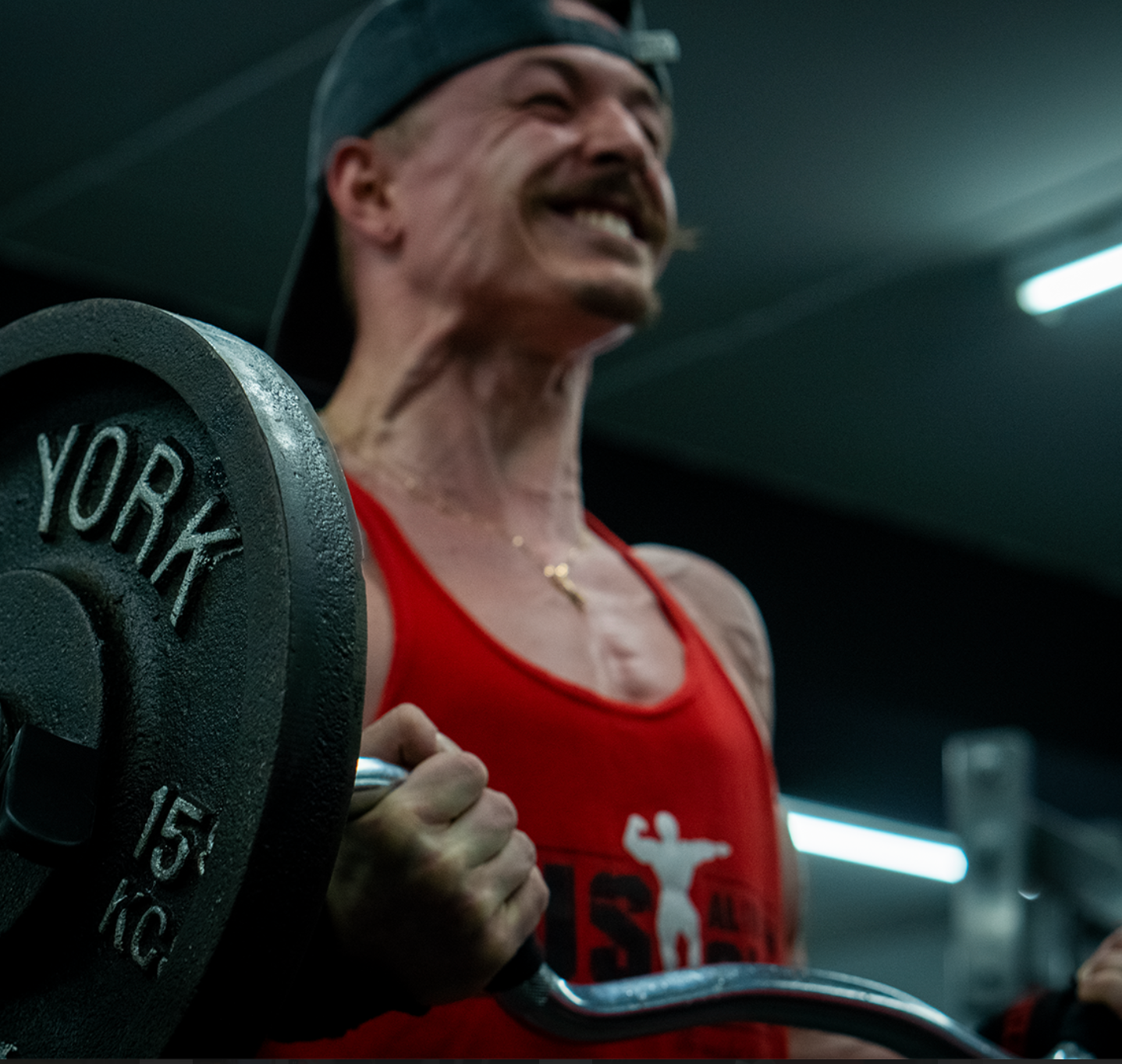 A man in a red tank top is lifting a york 15 kg barbell