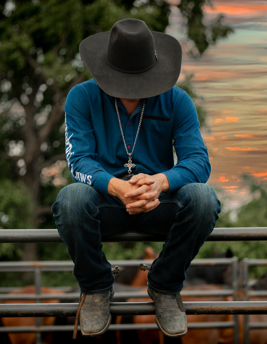 A man wearing a cowboy hat is sitting on a fence.