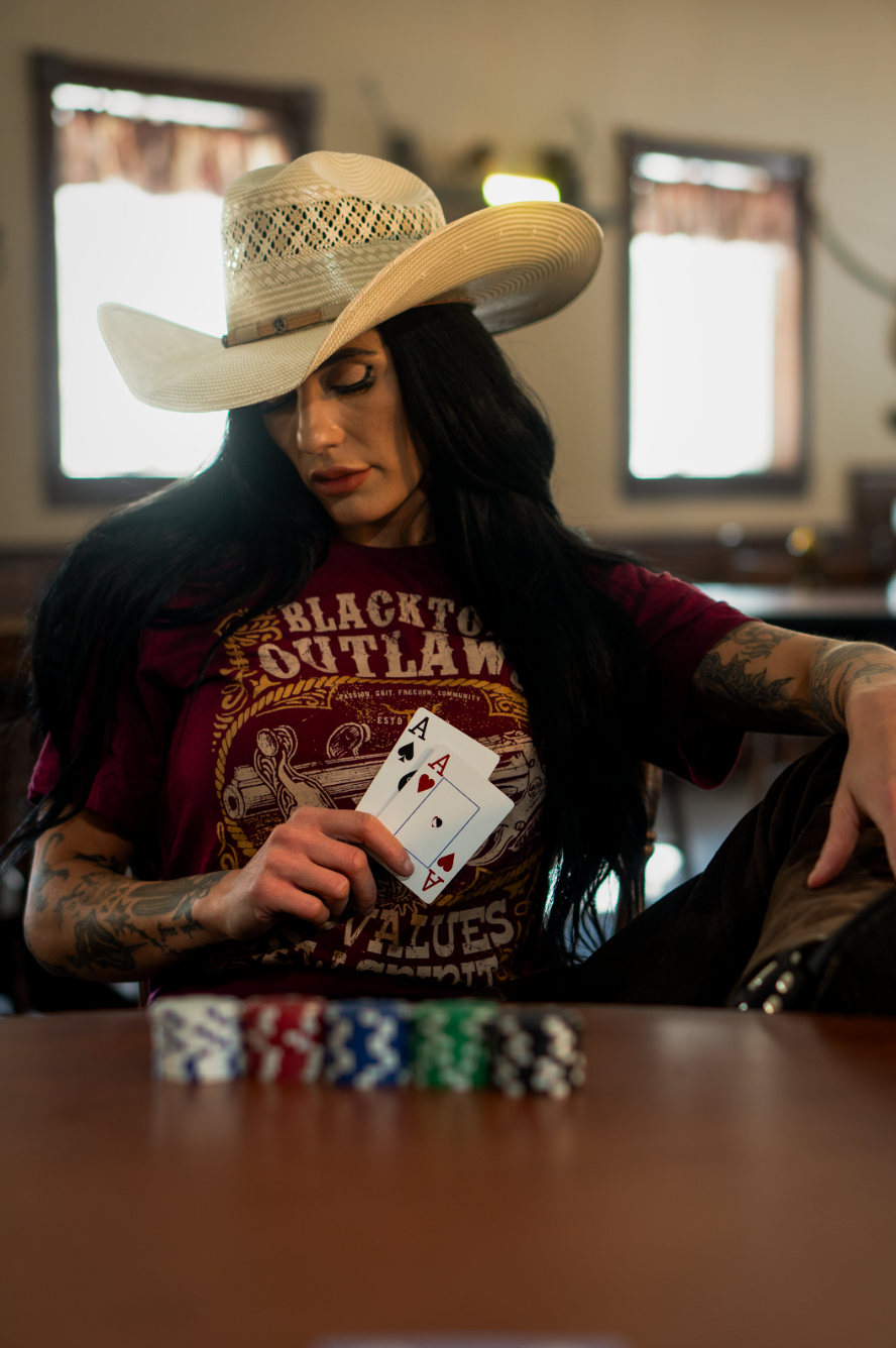A woman in a cowboy hat is sitting at a table holding a pair of aces.