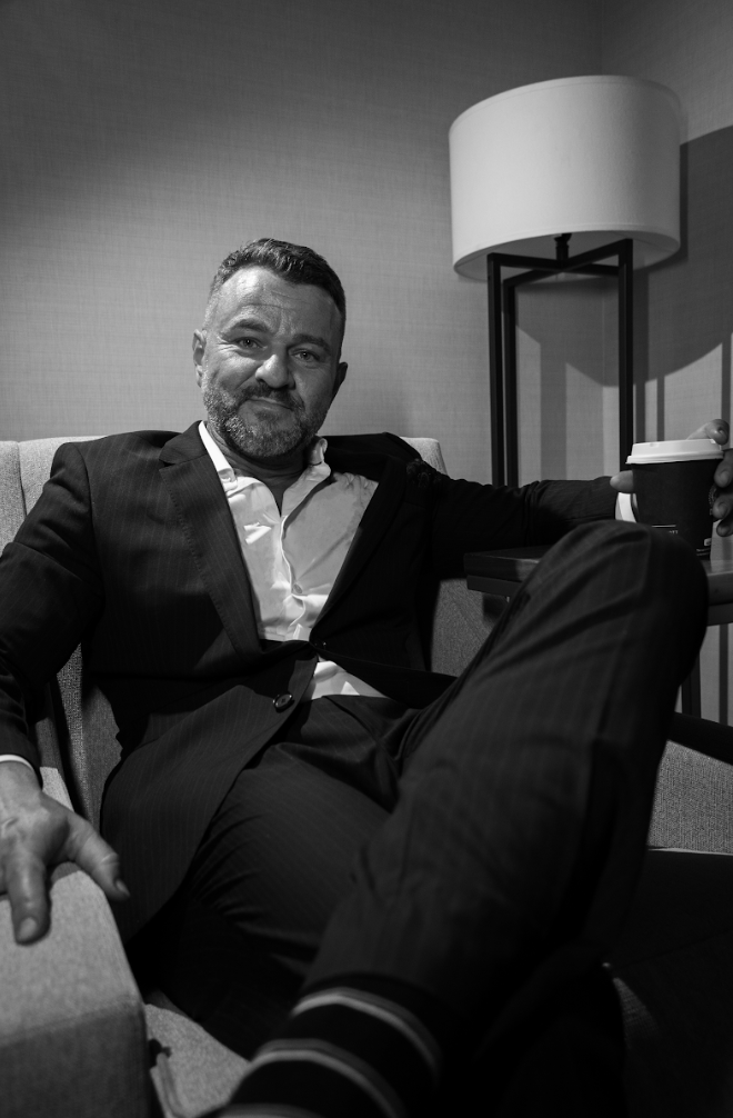 A man in a suit is sitting in a chair with his legs crossed.