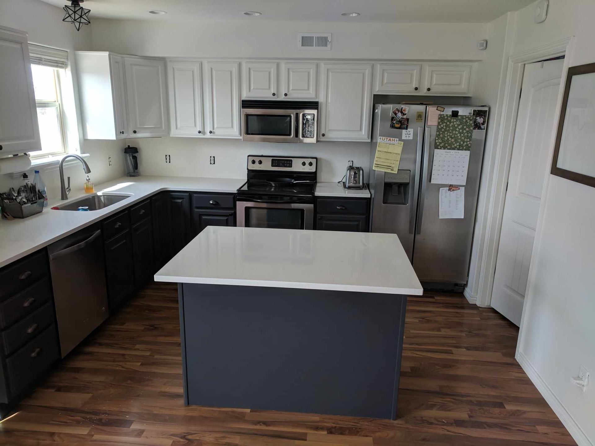A kitchen with white cabinets , stainless steel appliances , and a large island in the middle.