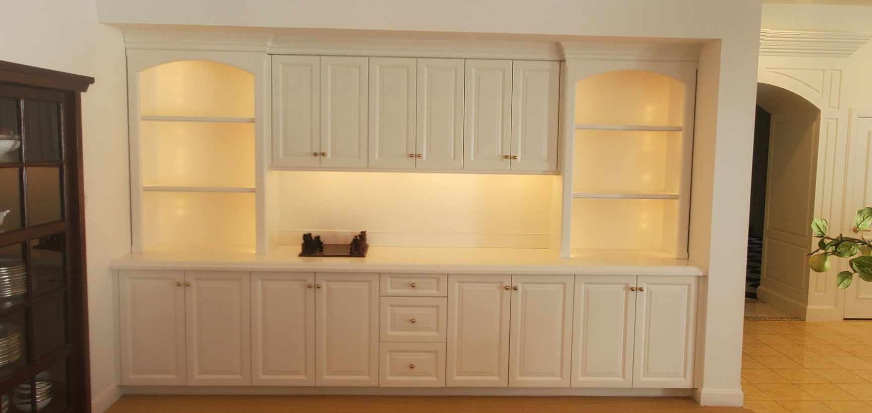 A living room with a lot of white cabinets and shelves.
