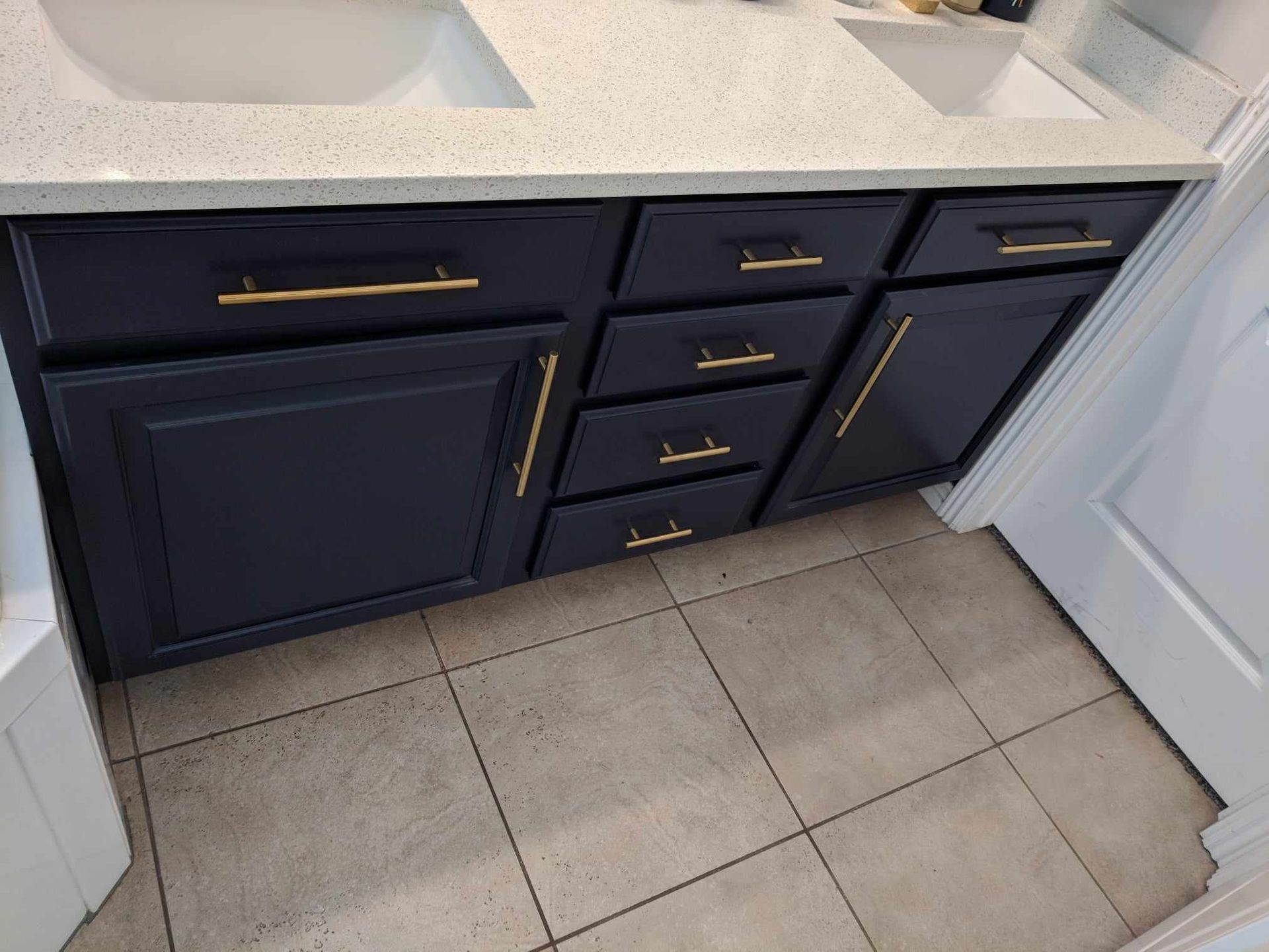 A bathroom vanity with black cabinets and gold handles.