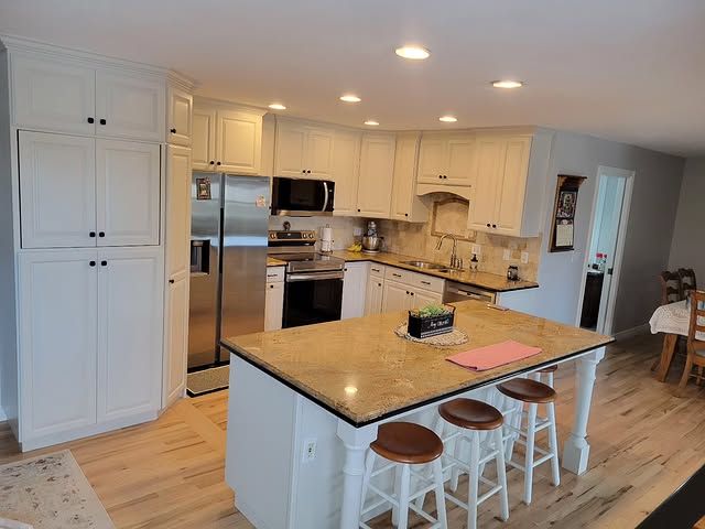 A kitchen with white cabinets , granite counter tops , stainless steel appliances and a large island.