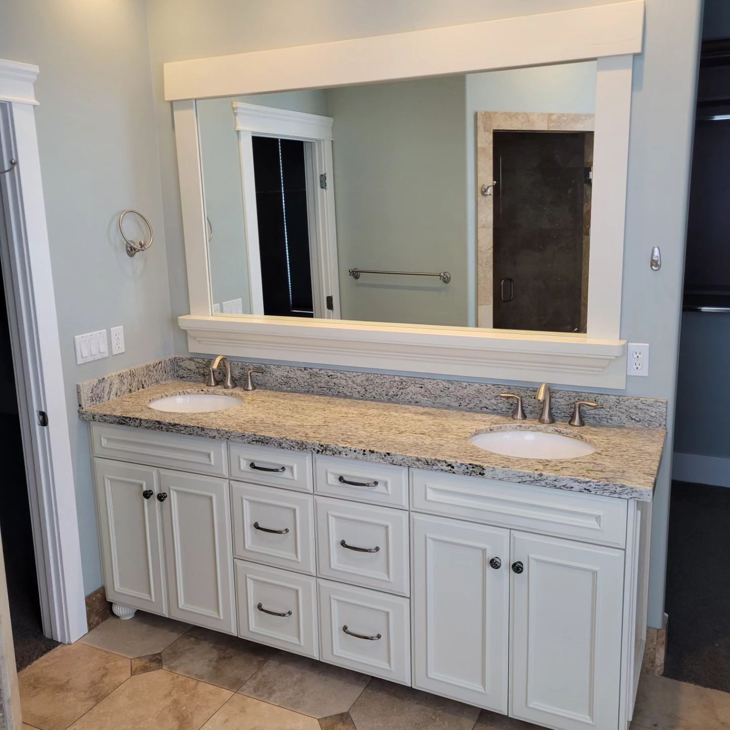 White bathroom vanity with two sinks, granite countertop, large mirror, and white trim.