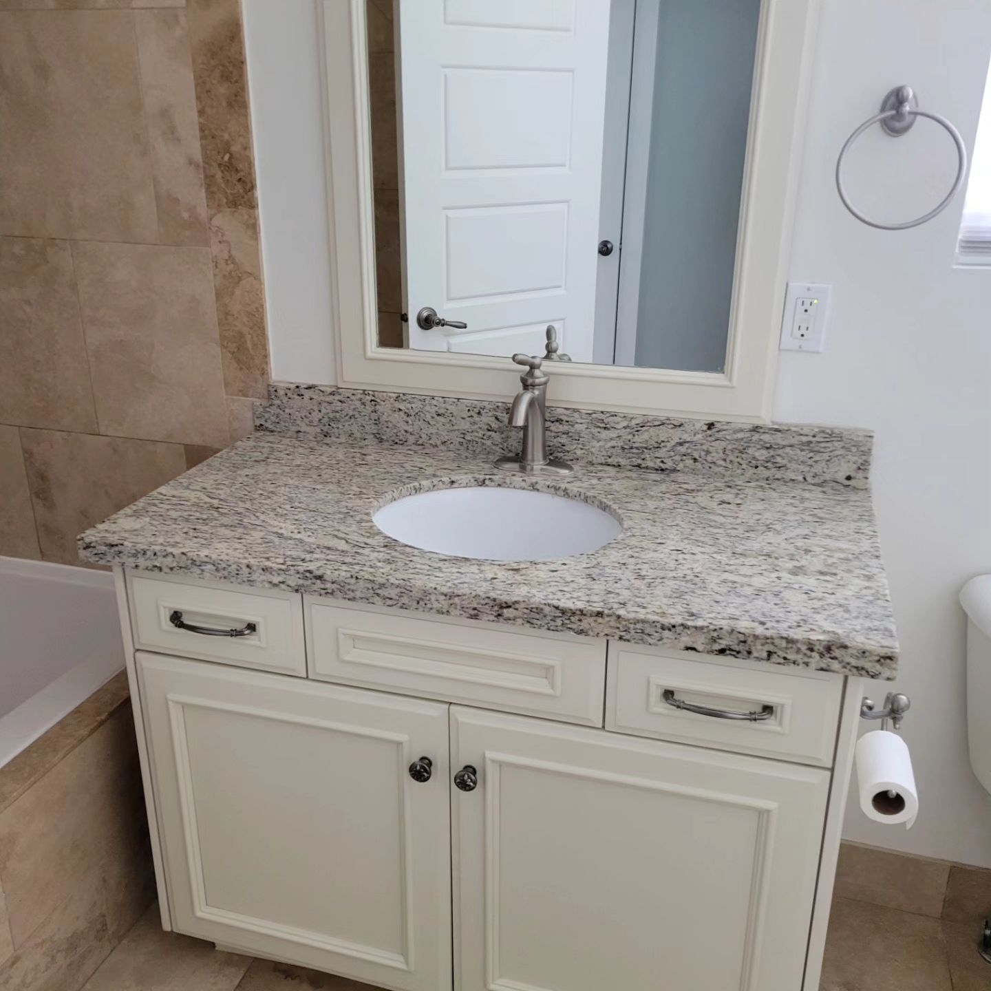 Bathroom vanity with granite countertop, cream-colored cabinet, white sink, and mirror.
