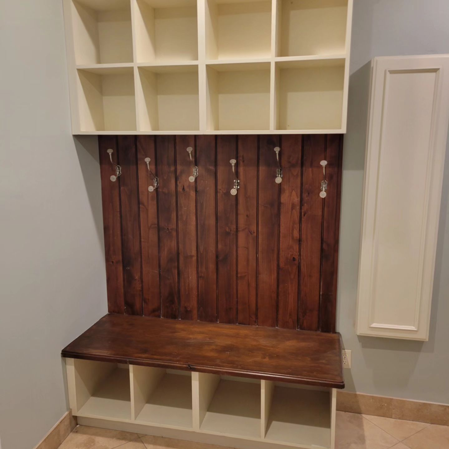 Entryway storage: light tan cubby shelves and bench with dark wood backboard and hooks