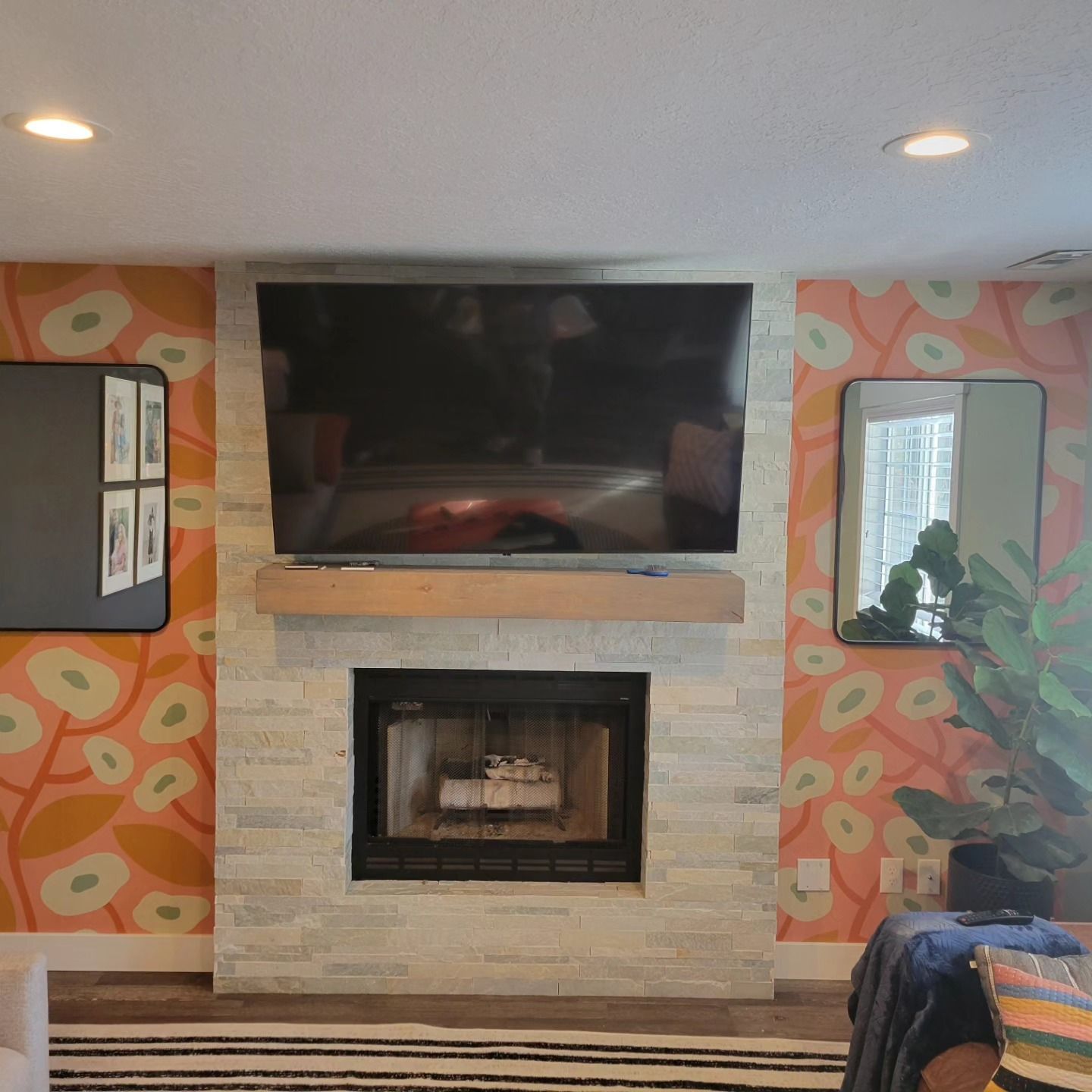 Fireplace with TV and mirror against floral wallpaper.