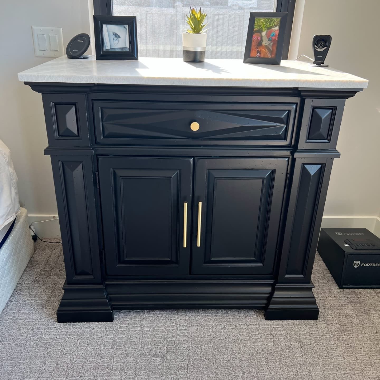 Black bedside table with gold hardware, white marble top, and decorative molding.
