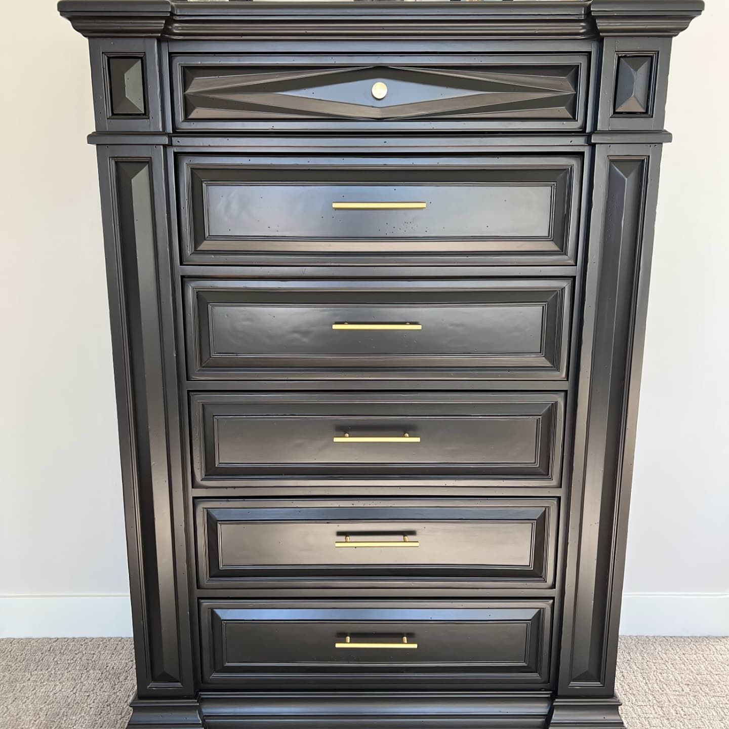 Tall, black dresser with six drawers, gold handles, and decorative trim.