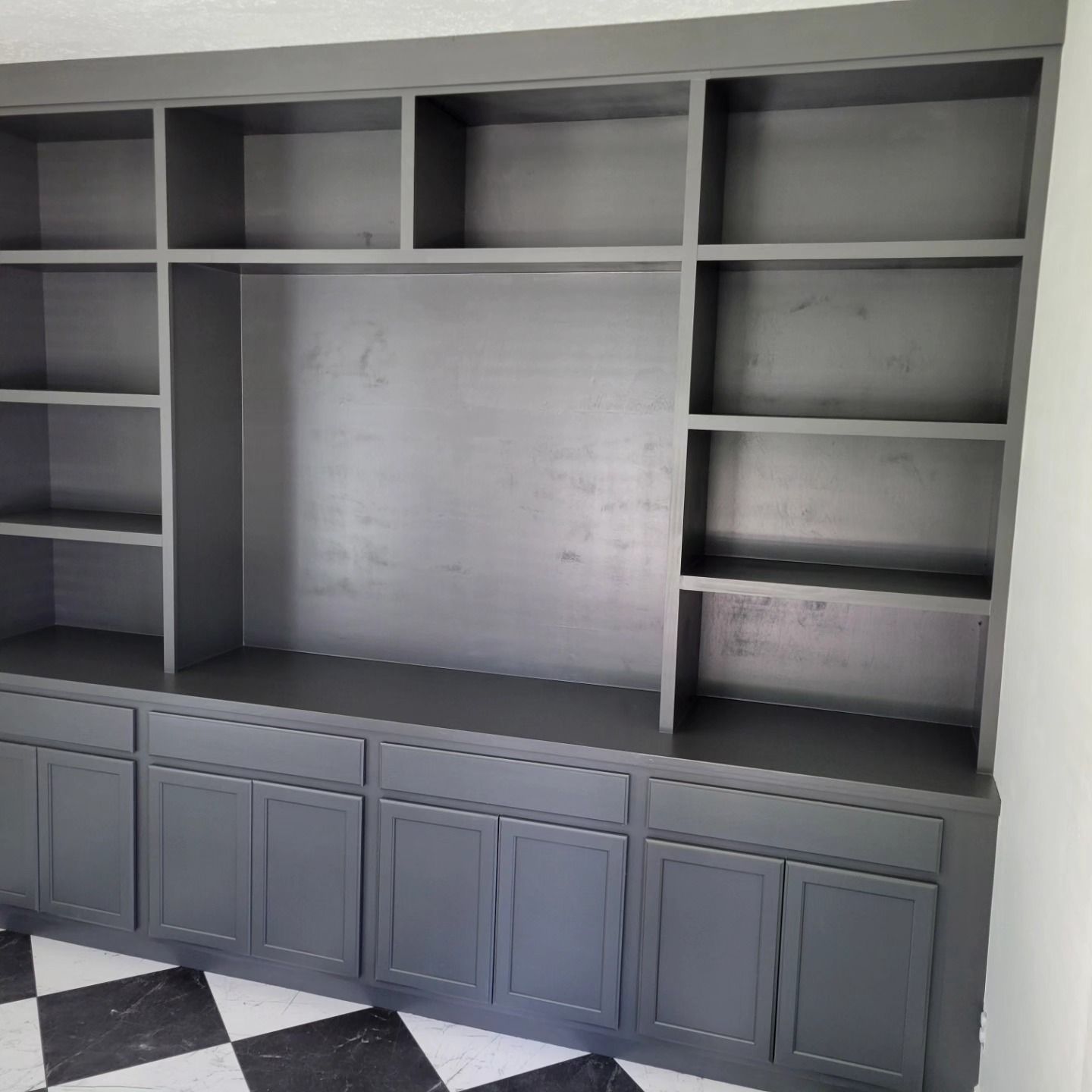Gray built-in cabinet with shelves and lower doors against a wall. Black and white checkered floor in front.