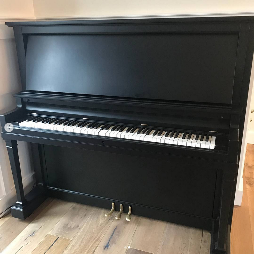 A black piano is sitting on a wooden floor in a room.