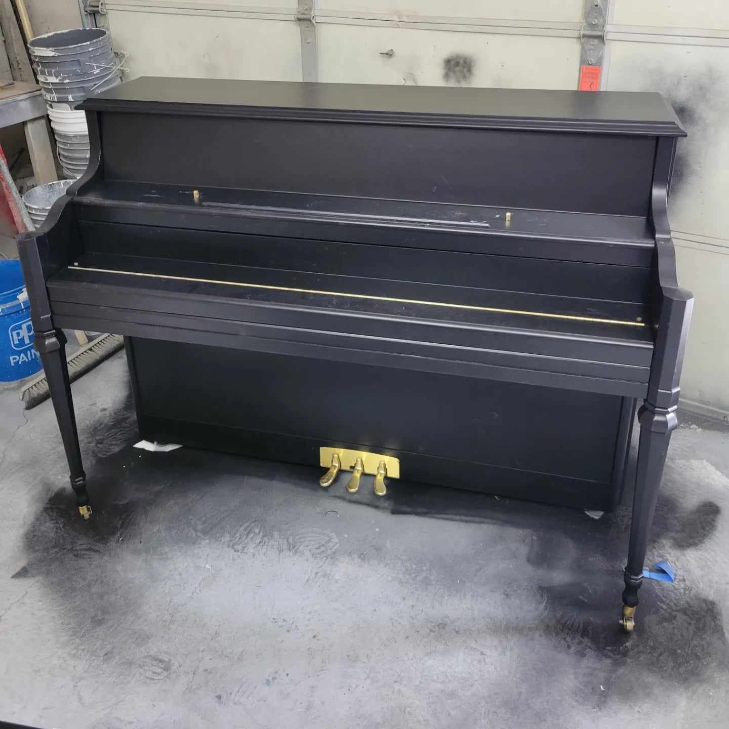 A black piano is sitting on a concrete floor in a garage.