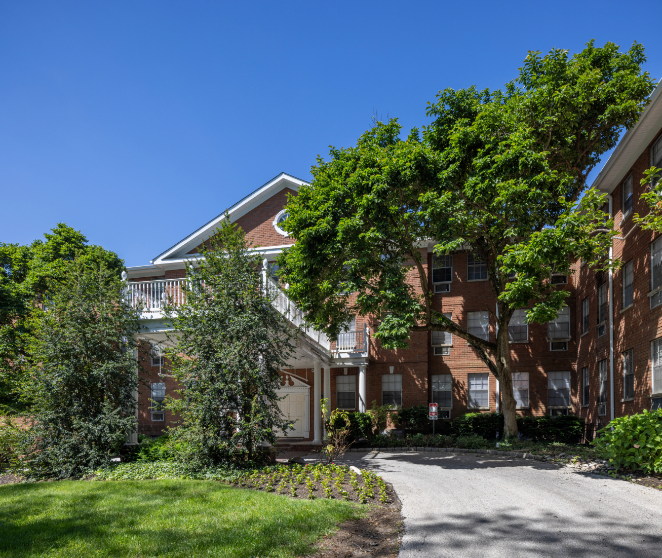 Brick apartment building with mature trees and a sunny, blue sky.