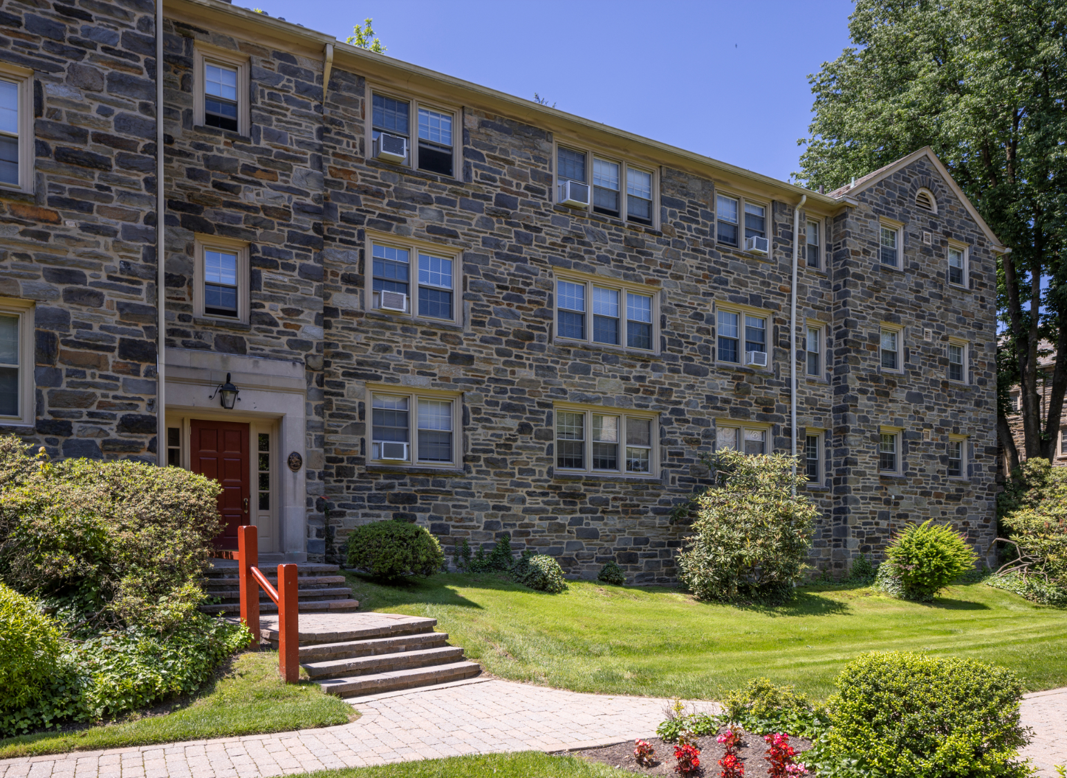 Three-story stone apartment building with red front door, windows, and green lawn.