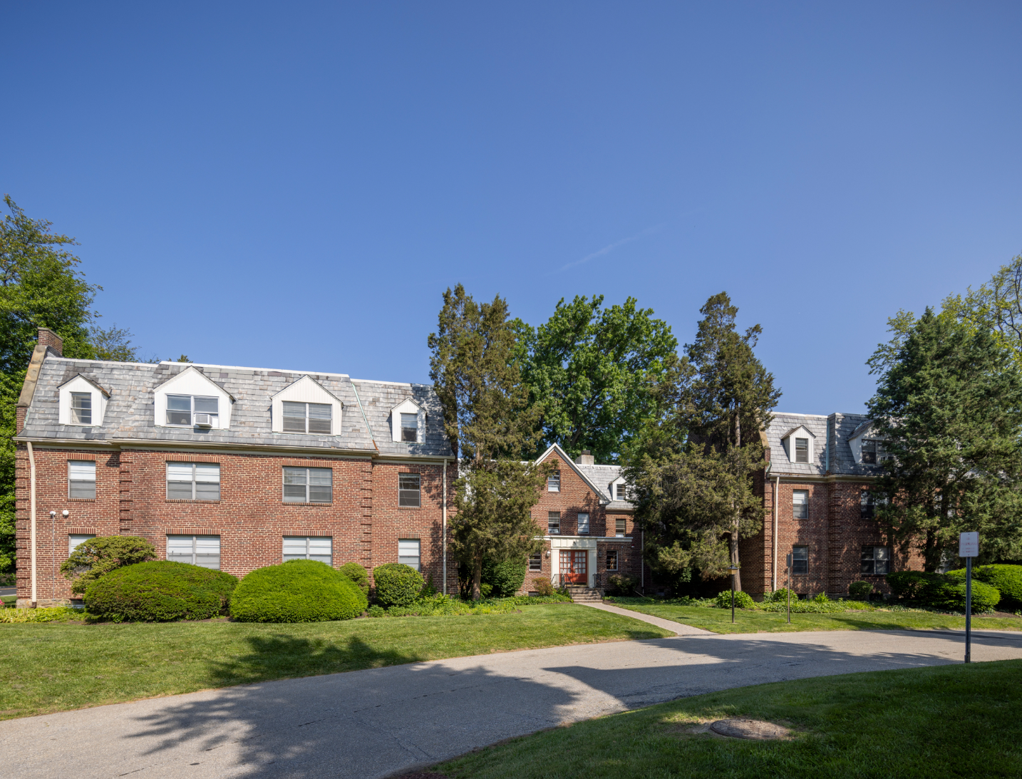 Red brick apartment building with white dormers, green lawn, and blue sky.