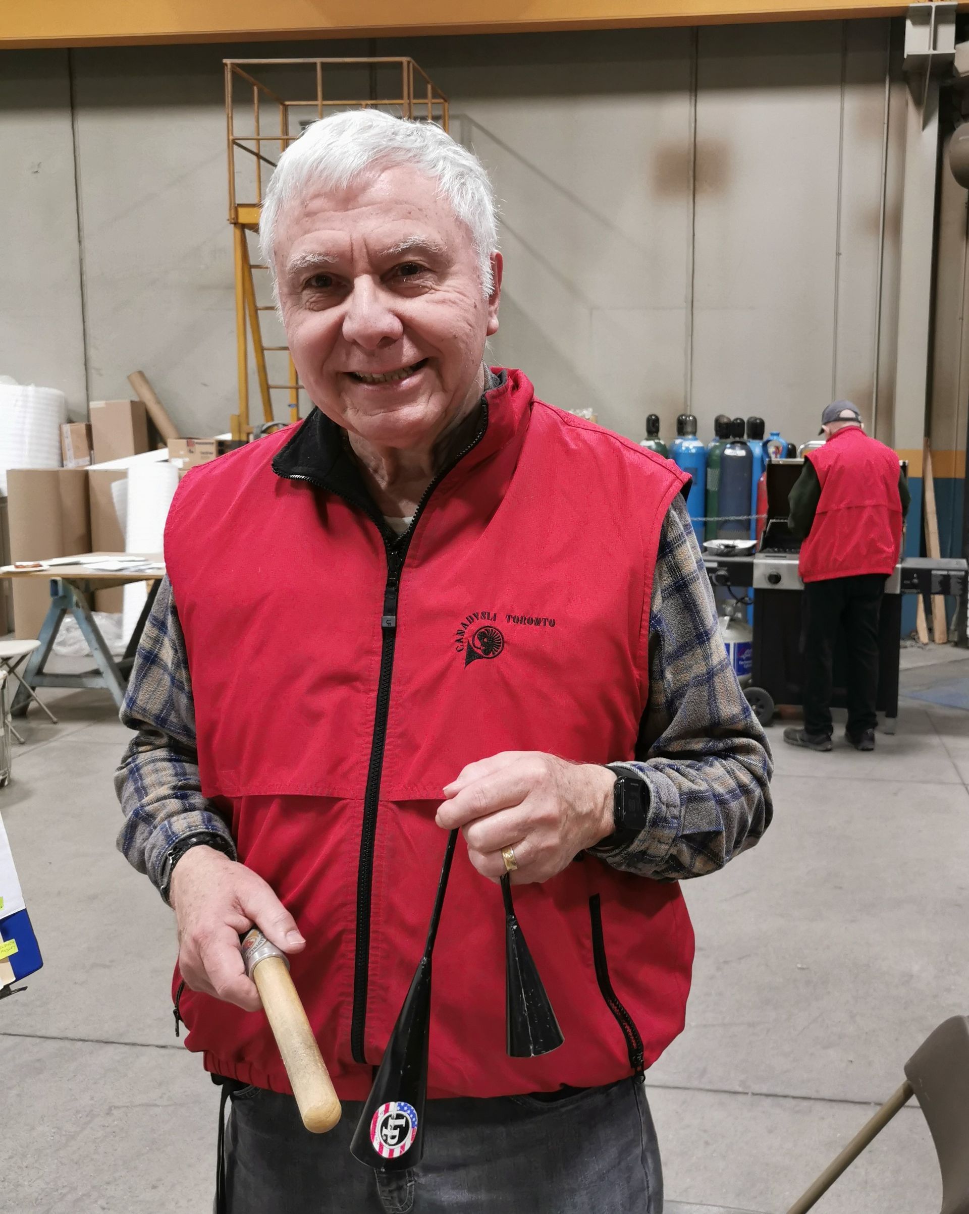 A man in a red vest is holding a wooden stick