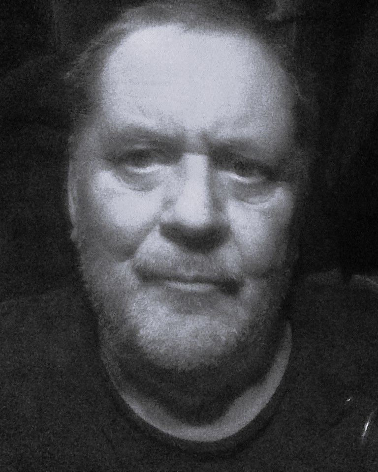 A man with a beard is looking at the camera in a black and white photo.