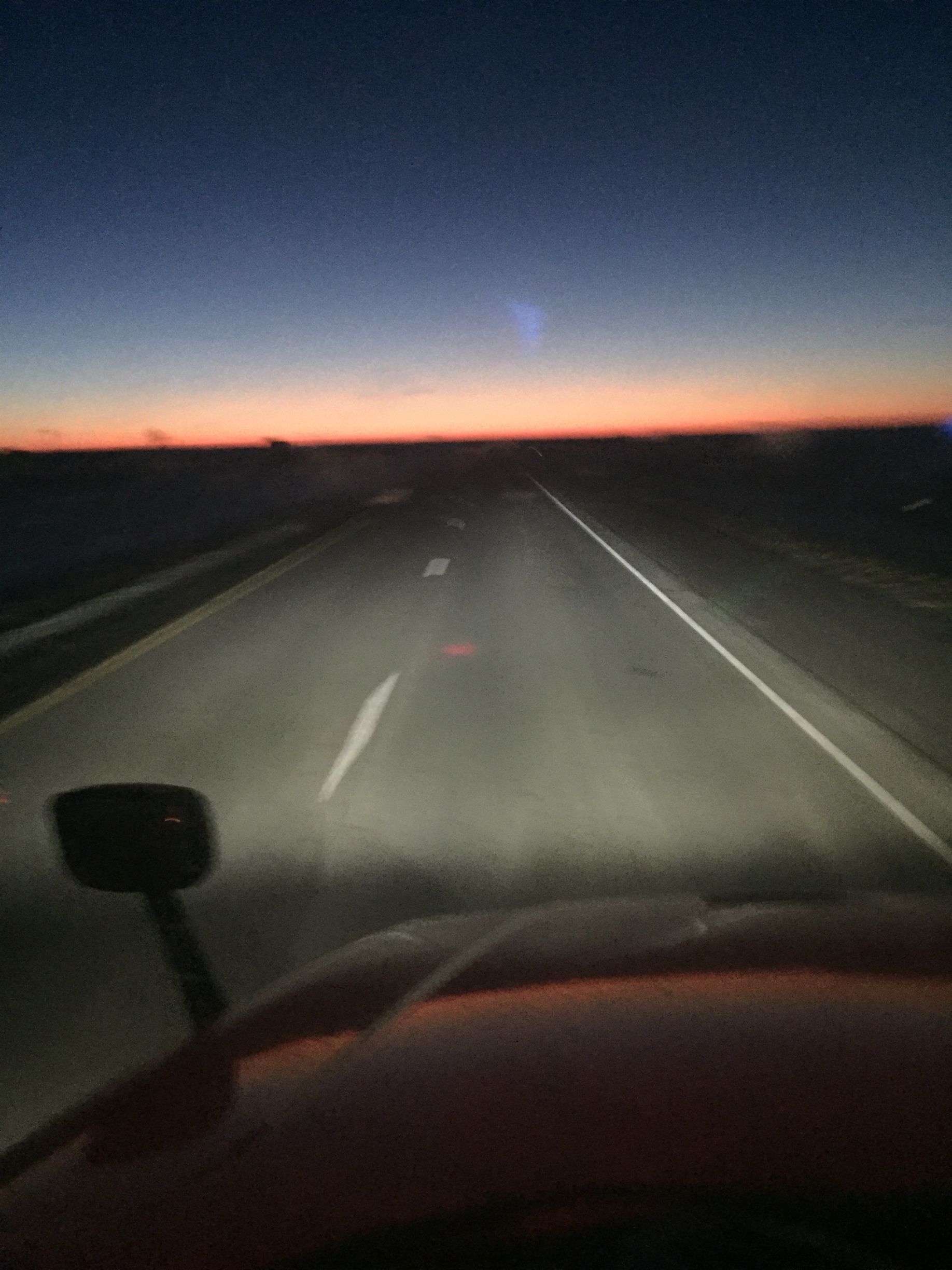 A car is driving down a highway at night with a sunset in the background.