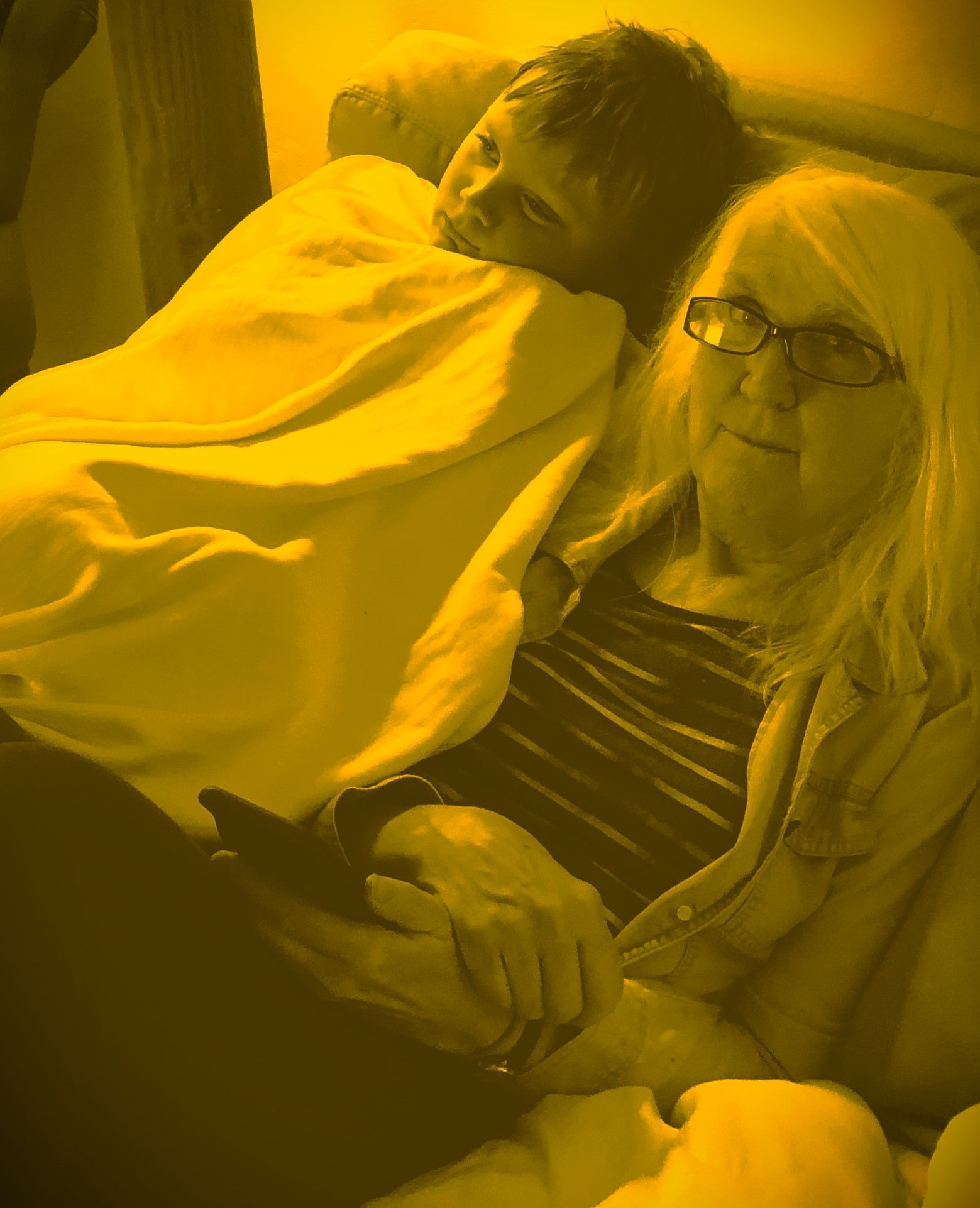 A woman and a child are laying on a couch under a blanket.