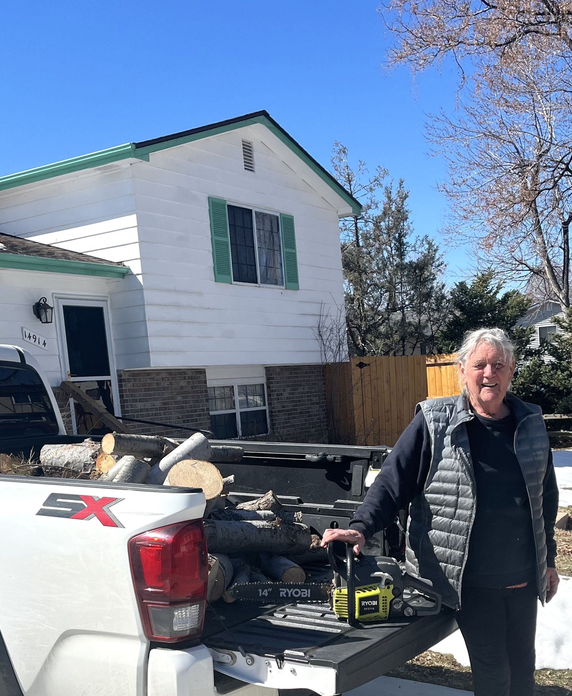 A man is standing next to a truck with a house in the background.