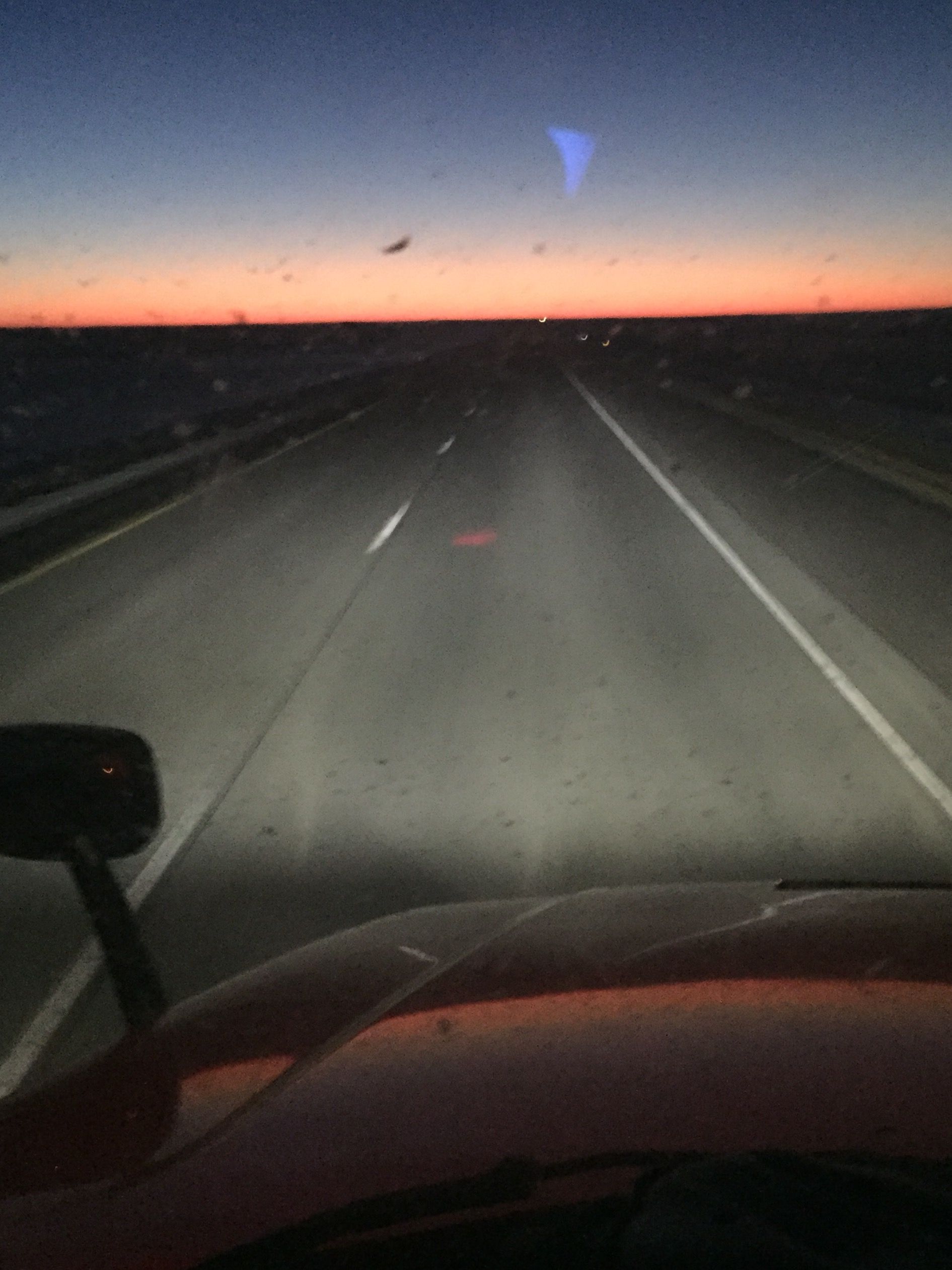 A car is driving down a highway at night with a sunset in the background.