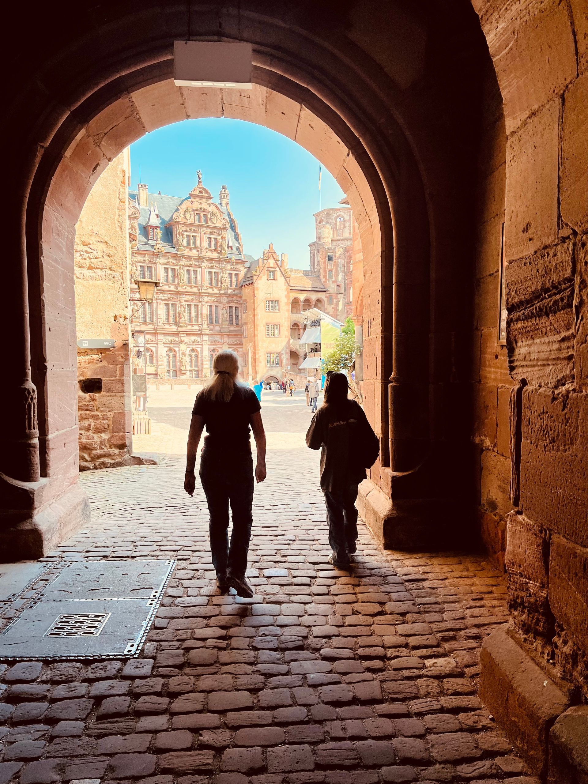 Two men are walking through a stone archway.