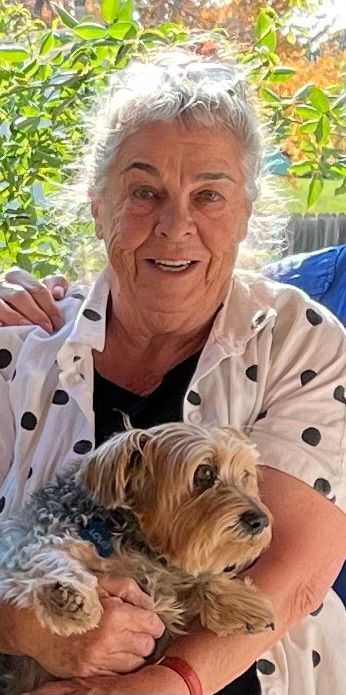 An elderly woman is holding a small dog in her arms.