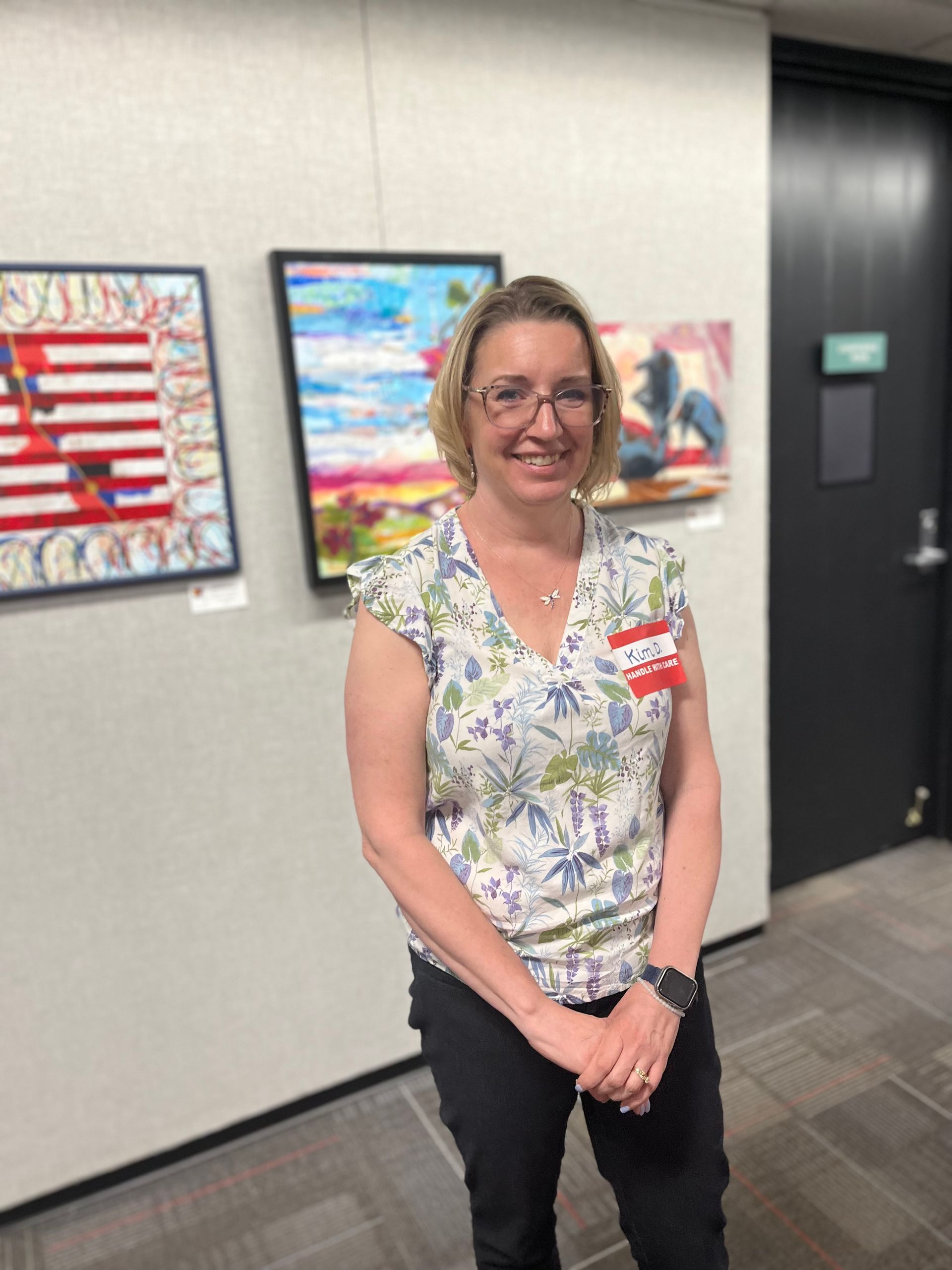 A woman is standing in front of a wall with paintings on it.