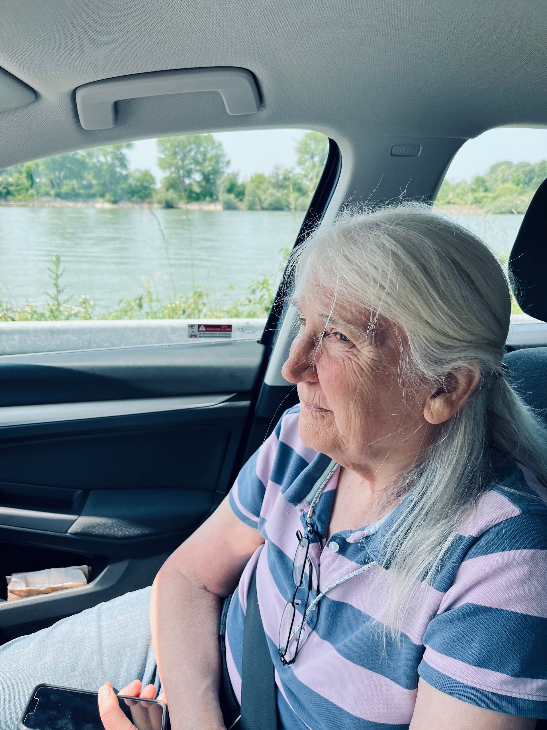 An elderly woman is sitting in the back seat of a car looking out the window.