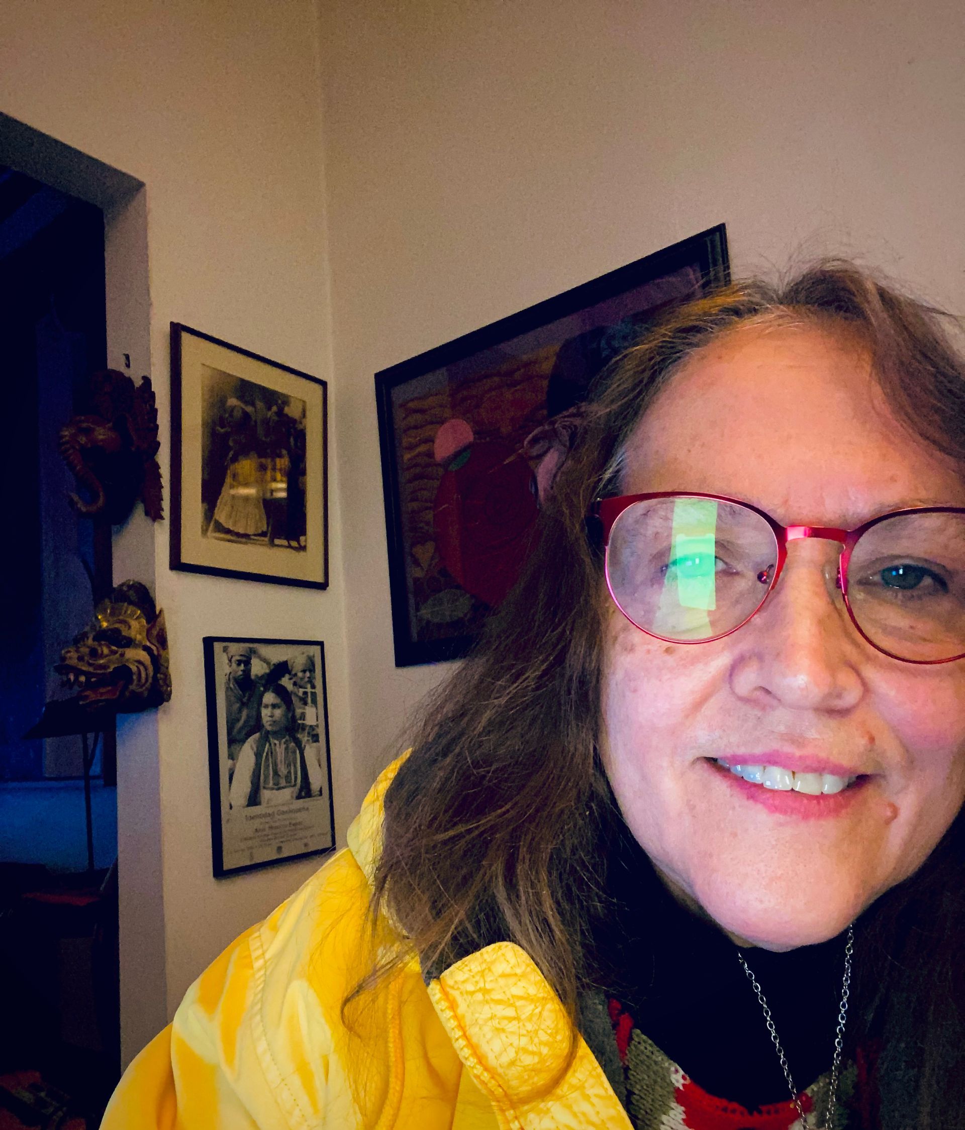 A woman wearing glasses and a yellow jacket is smiling for the camera.