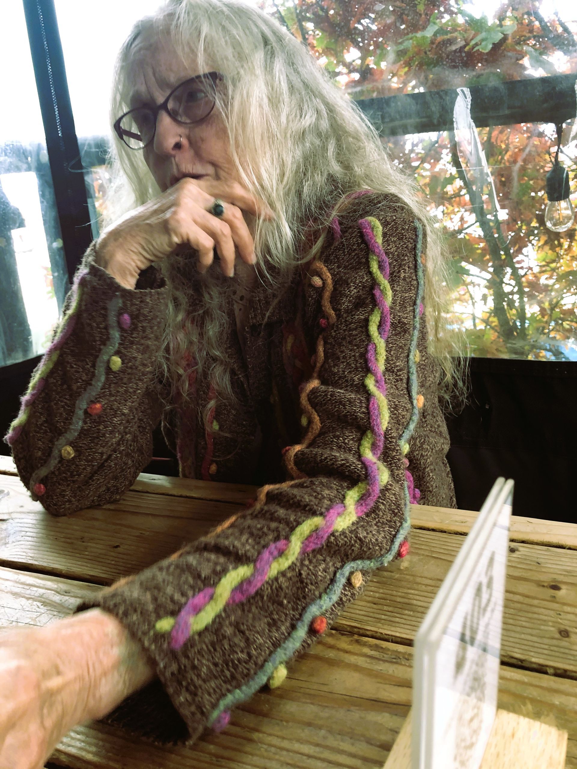 A woman wearing glasses sits at a table with her hand on her chin