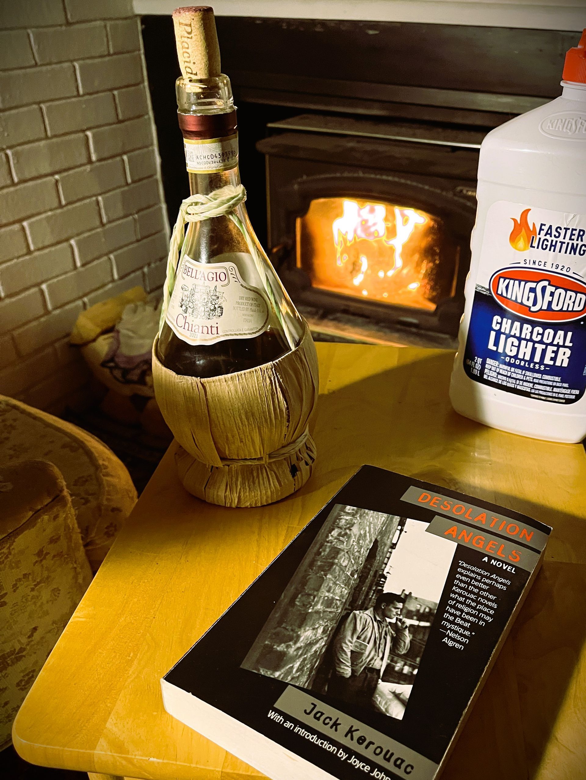 A bottle of wine sits next to a book and a bottle of charcoal lighter