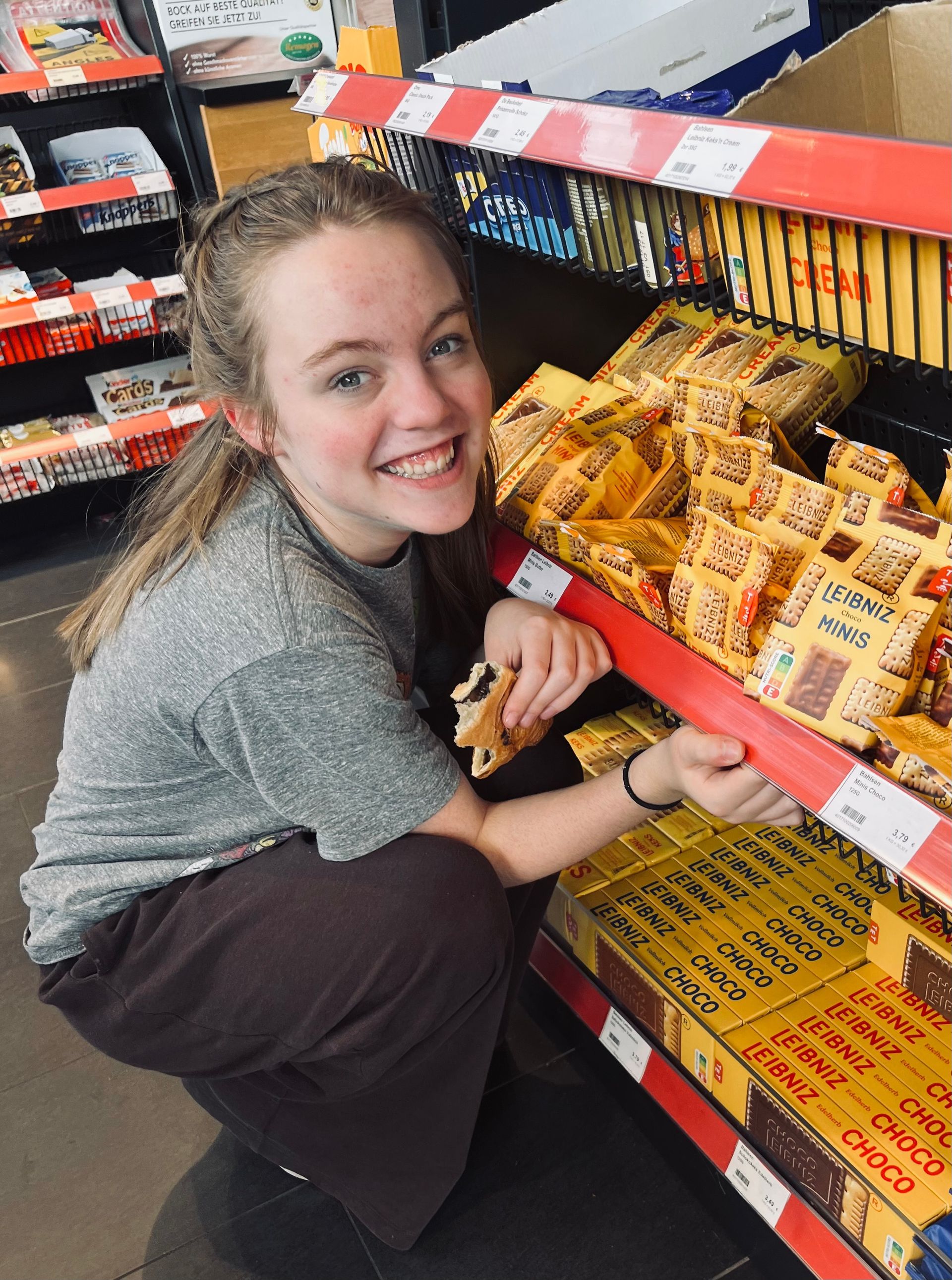A woman is kneeling down in front of a shelf of food in a store.
