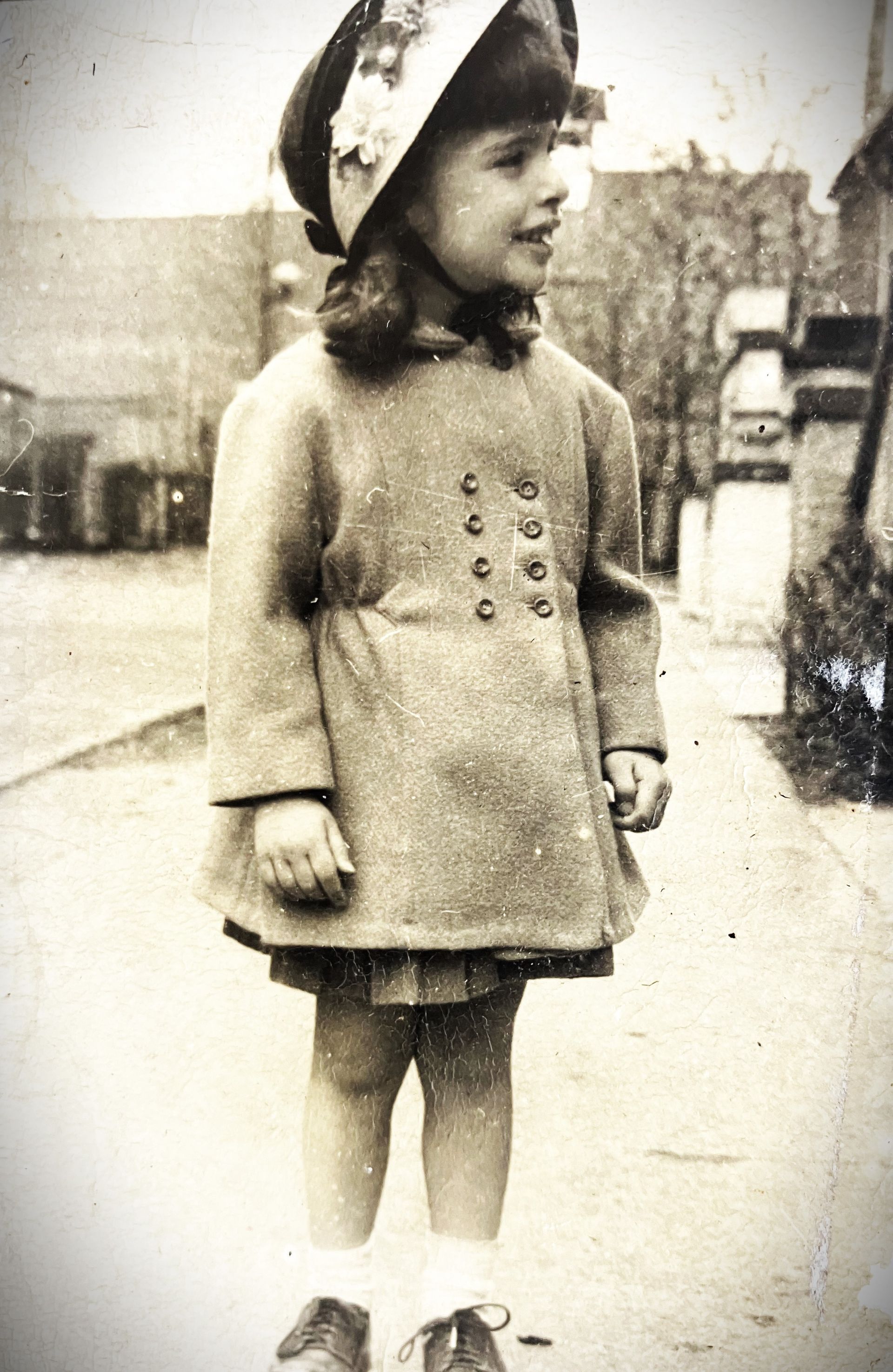 A black and white photo of a little girl wearing a hat and coat