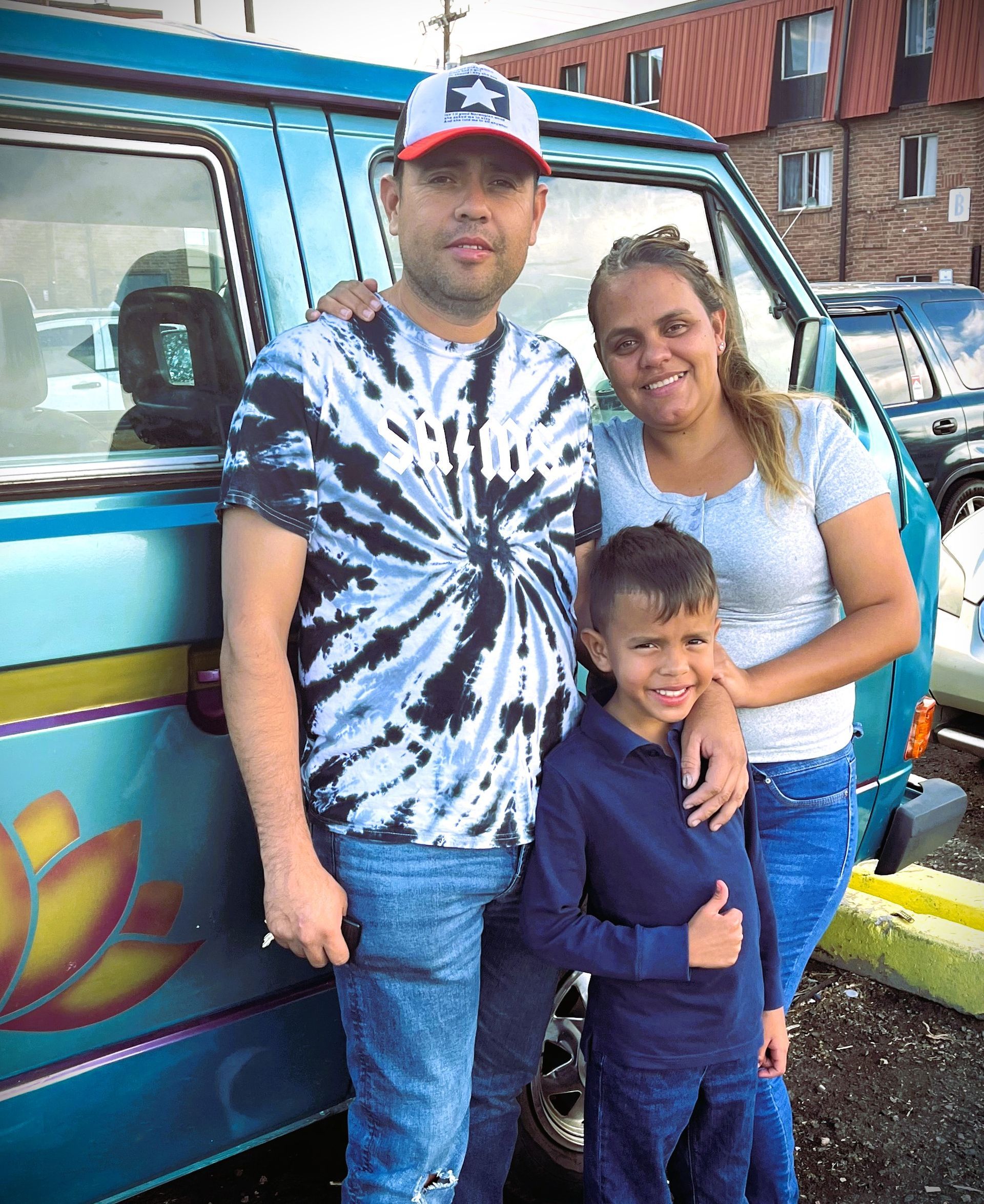 A man , woman and child are posing for a picture in front of a blue van.