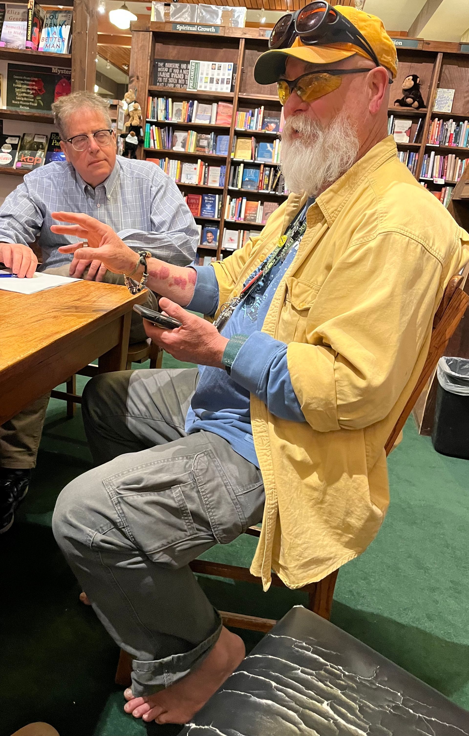 A man with a beard is sitting at a table in a bookstore.