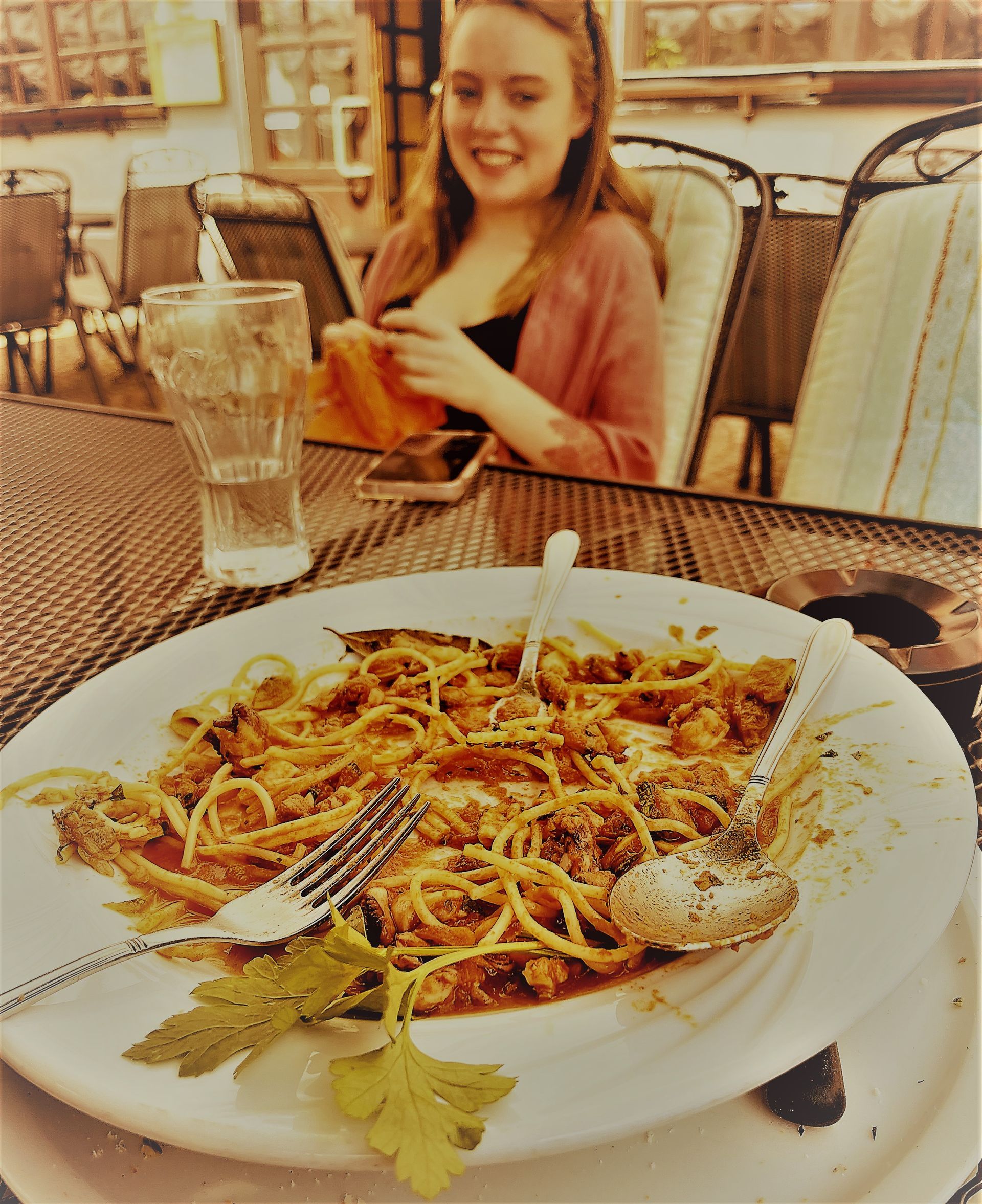 A woman sits at a table with a plate of spaghetti and a glass of water