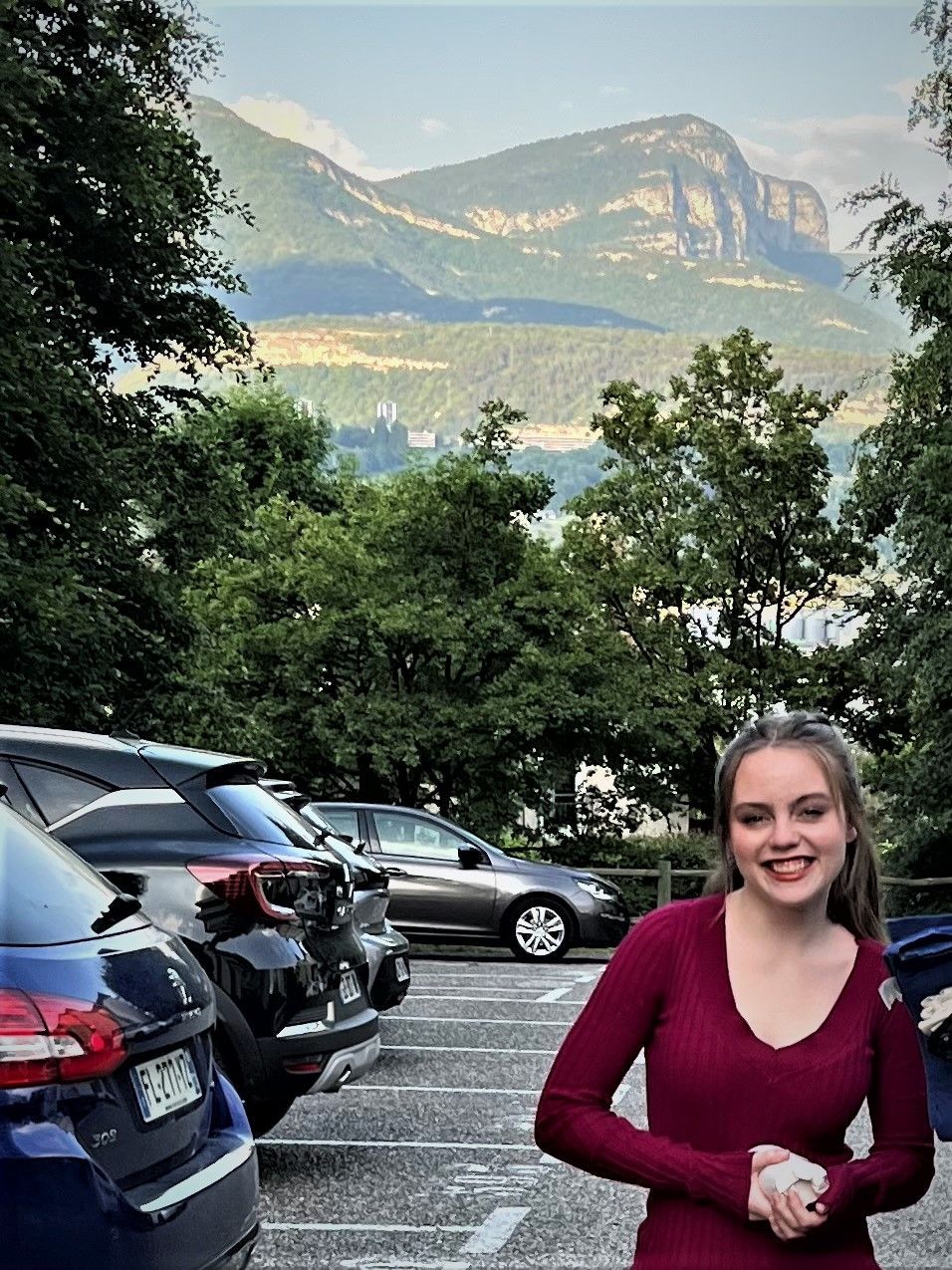 A woman is standing in a parking lot with mountains in the background.