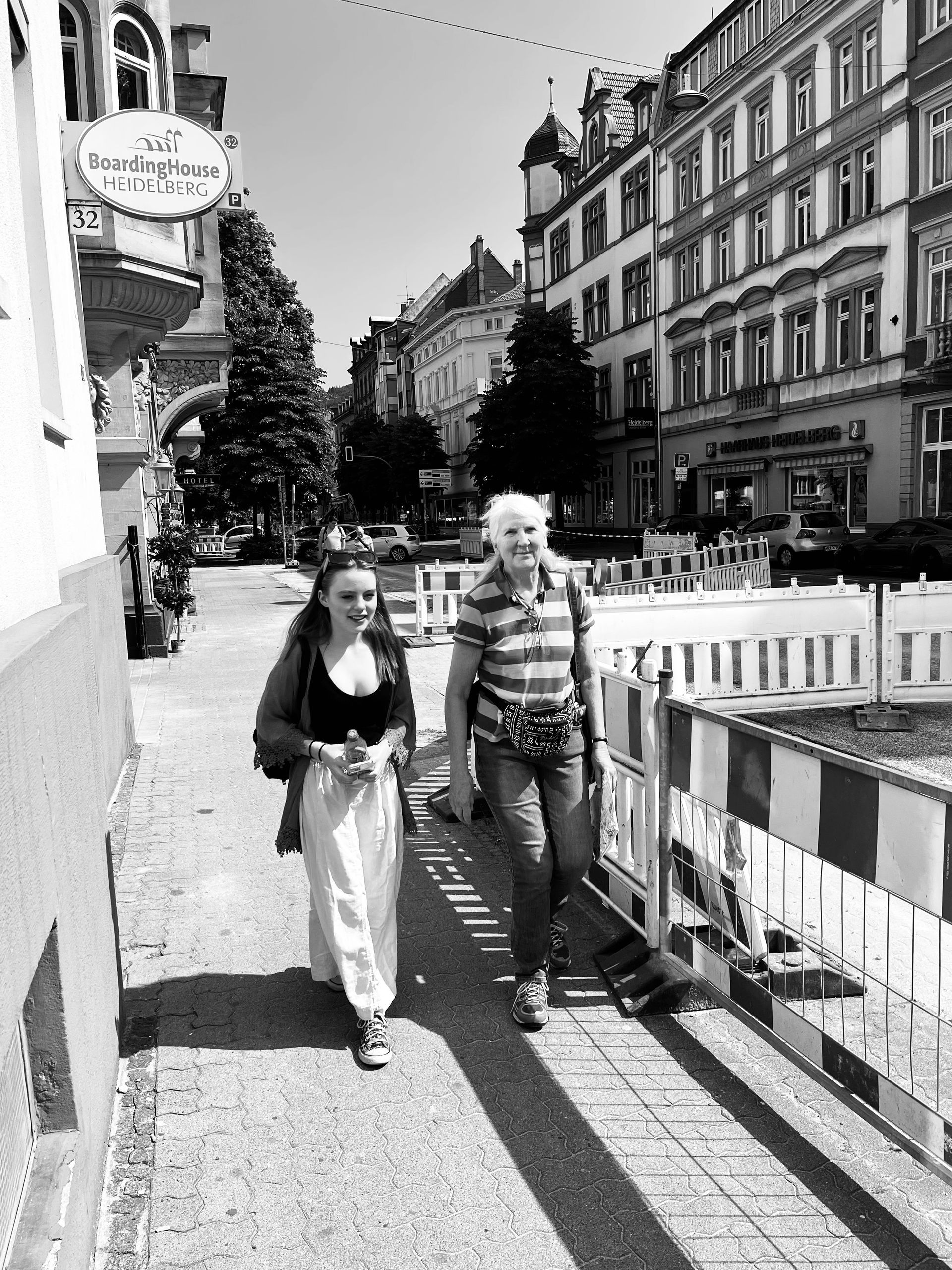 Two women are walking down a sidewalk in a black and white photo.