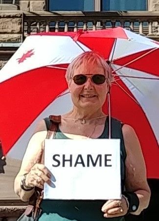A woman is holding a sign that says `` shame '' under an umbrella.