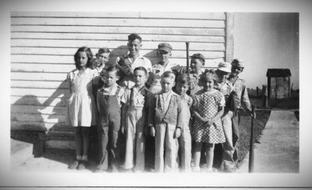 A black and white photo of a group of children standing in front of a building.